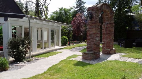 Romantischer Torbogen im Garten mit Wintergarten im Hintergrund – perfekte Kulisse für deinen Aufenthalt in einem exklusiven BDSM Ferienhaus